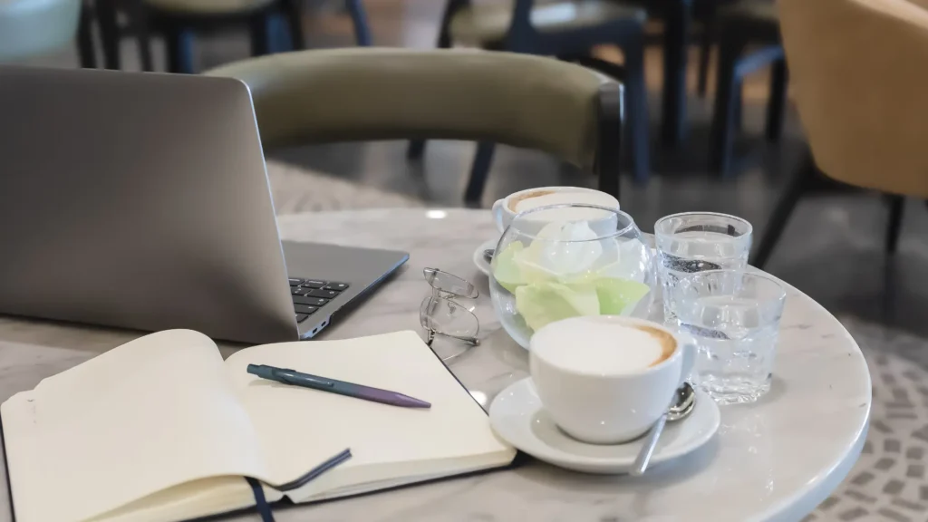 cafe table set up with a laptop, notebook, and coffee